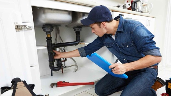A plumber checking a job on a tablet under a kitchen sink