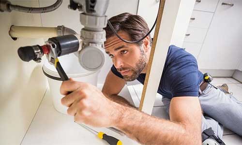 A plumber fixing pipework under a sink